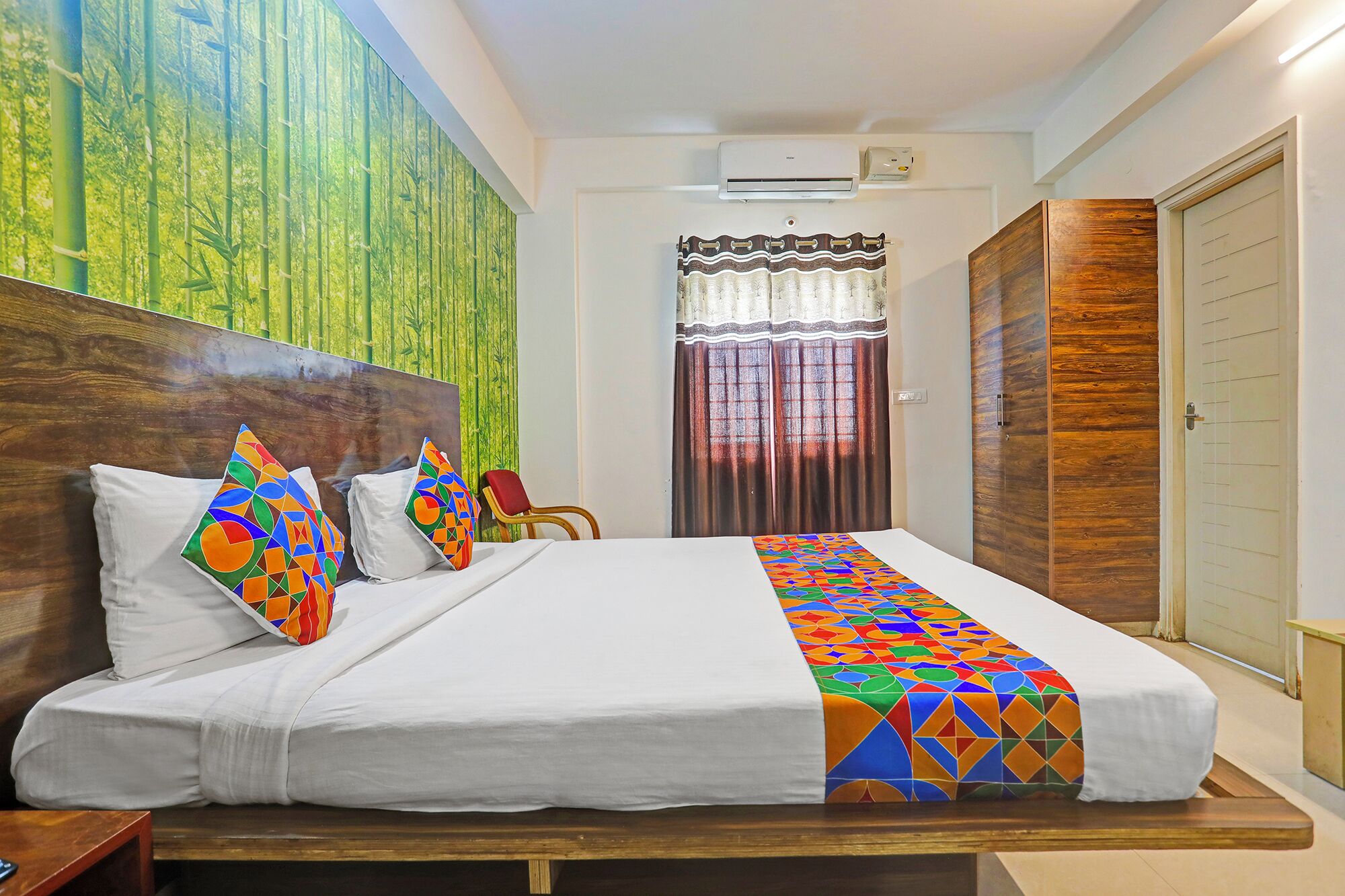 Una cama bien tendida con una colcha de estampado geométrico, un cabecero de madera y una pared con papel tapiz de bambú.