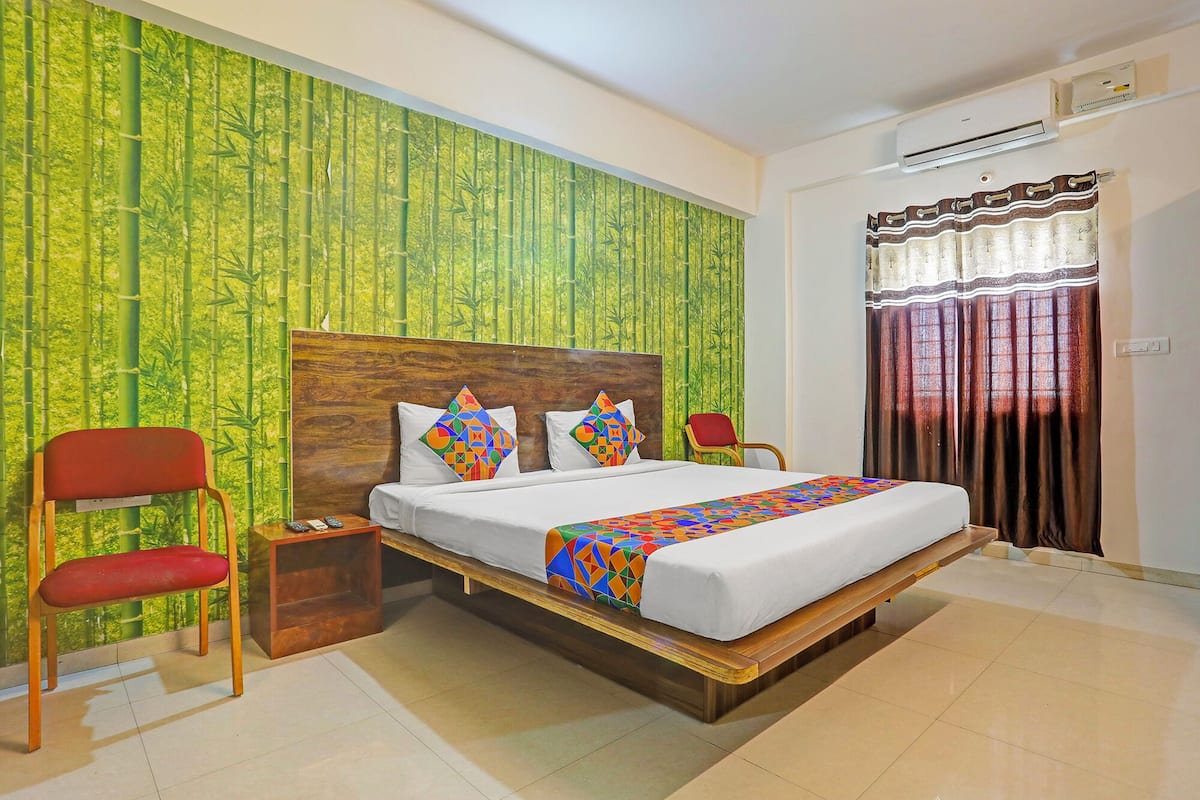 Quarto com cama, duas cadeiras, mesa de cabeceira e janela com cortinas.