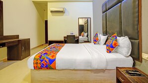A hotel room with a large bed, a desk, a chair, a wardrobe, and an air conditioning unit. - Fabhotel Balaji Resort (Calangute)