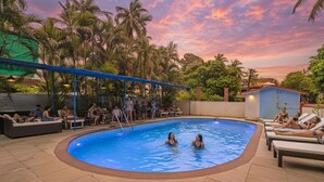 A swimming pool with lounge chairs and a covered seating area, surrounded by palm trees and a sunset sky. - Fabhotel Balaji Resort (Calangute)