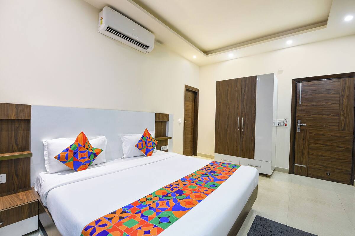 A hotel room with a bed, two pillows, a colorful bed runner, a wardrobe, and a door.