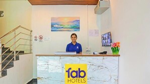 A hotel reception desk with a marble counter, a receptionist, a painting of a sunset, and a staircase to the left. - FabHotel Sujatha Residency - Near Channasandra Railway Station (Bengaluru)