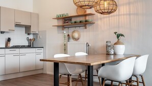 A modern kitchen with white cabinets, a wooden table, and two white chairs. There are hanging lights, a shelf with bowls, and a sign that says "SEAFOOD". - Beautiful Apartment With Harbour Views (The Hague)