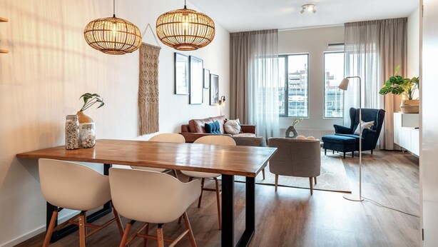 A modern living room with a wooden dining table, white chairs, a blue armchair, and a floor lamp. - Beautiful Apartment With Harbour Views (The Hague)