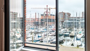 A room with a large window overlooking a marina with boats and buildings in the background. - Beautiful Apartment With Harbour Views (The Hague)