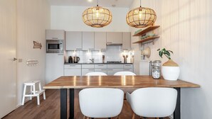 A modern kitchen with white cabinets, a wooden dining table, and two white chairs. There are two wicker pendant lights hanging above the table. - Beautiful Apartment With Harbour Views (The Hague)