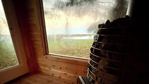 Una habitació amb una llar de pedra, sòls de fusta i vista a una zona verda a través d'una porta de vidre.
