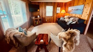 Habitació d'estil cabana acollidora, amb parets de fusta, un sofà, dos seients còmodes, una taula de cafè i un televisor fixat a la paret.