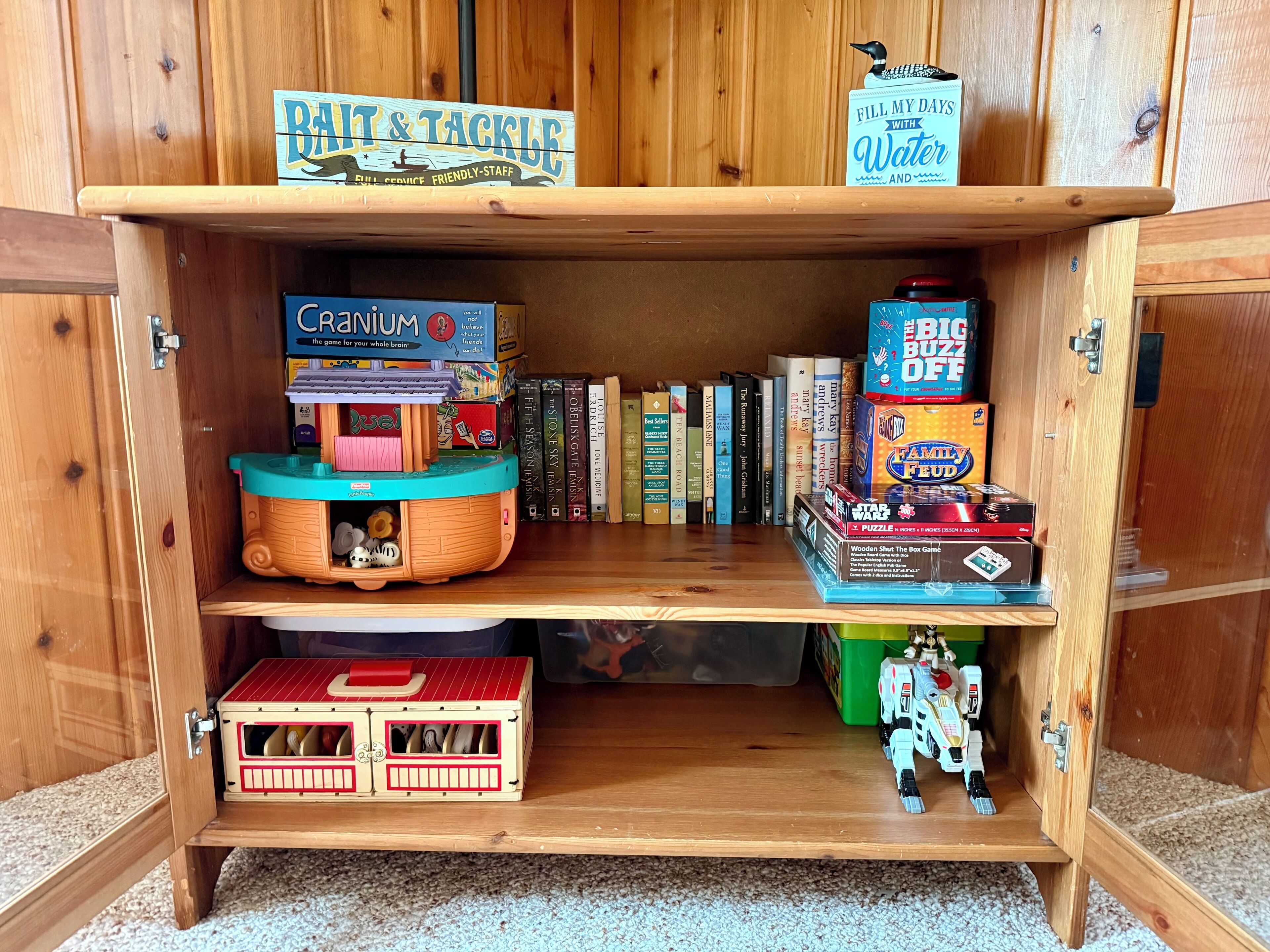 A wooden cabinet with shelves containing board games, books, and a toy train.