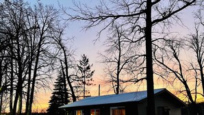 Una cabana amb terrassa, envoltada de terra coberta de neu i arbres sense fulles, sota un cel serè.