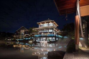 Un edificio a più piani con uno stile architettonico tradizionale, caratterizzato da ampie finestre e una piscina specchiante di fronte.