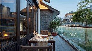 A modern outdoor dining area with a table set for two, overlooking a calm water body and a traditional building in the background. - MOONRISE HOTELS & RESORTS (Deyang)