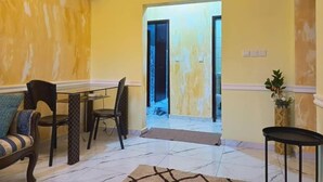 Una habitación con una pared amarilla, una mesa de comedor con sillas, un sofá, una mesita negra y una planta en maceta.