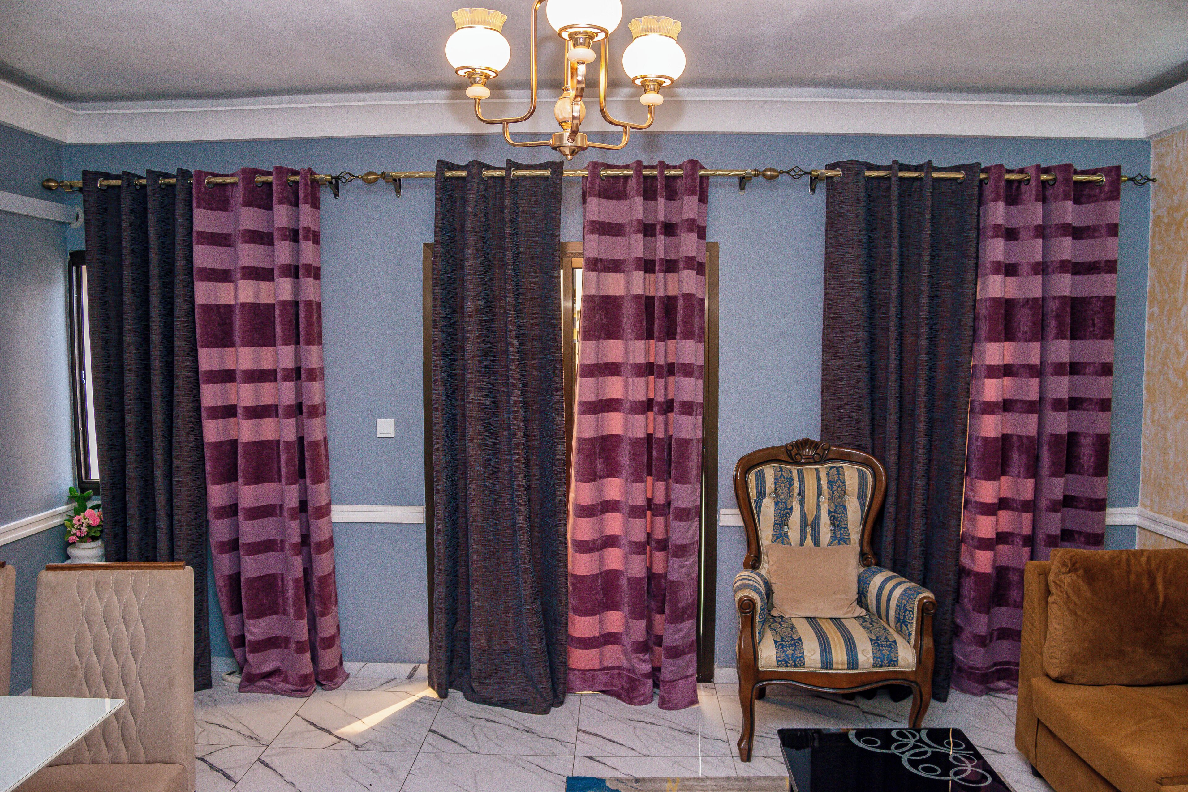 A room with a blue wall, a wooden chair with a striped cushion, a brown sofa, and a chandelier.
