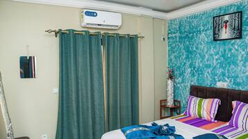 Una habitación de hotel con cama, cortinas, aire acondicionado, un cuadro enmarcado y un jarrón con flores.