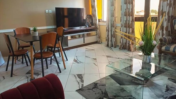 Una sala de estar con televisión, mesa de comedor, sillas y una mesa de centro de vidrio.