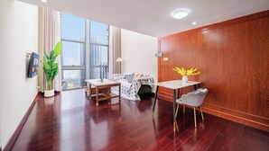 A modern hotel room with a large window, a wooden wall panel, a dining table with a chair, a small sofa, and a potted plant. - Guangzhou Duoya Intl. Service Apartment (Guangzhou)