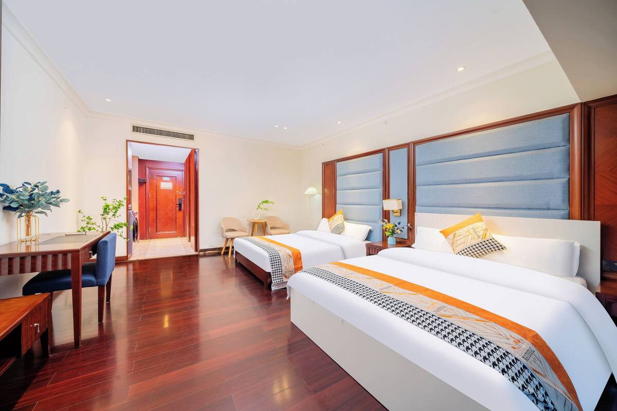 A hotel room with two beds, a desk, and a chair.