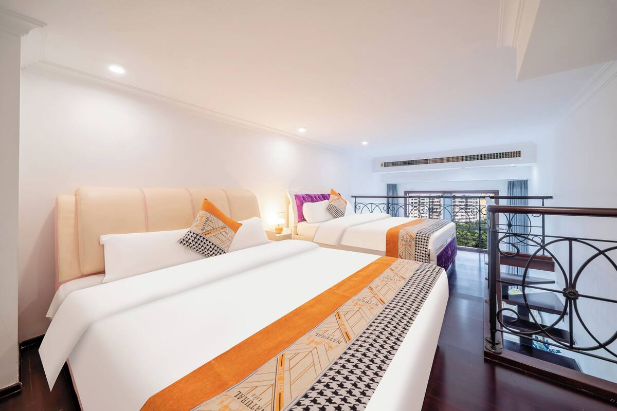 A hotel room with two beds, a balcony with a wrought iron railing, and a view of the cityscape.