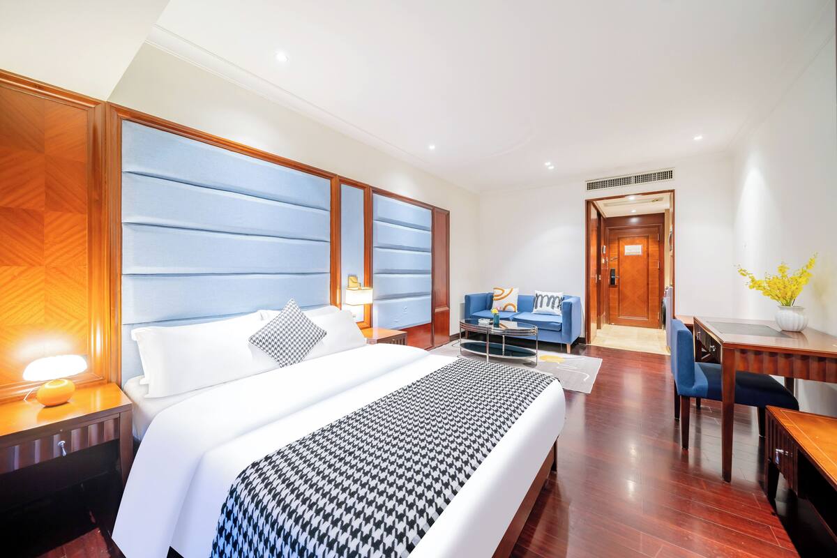 A hotel room with a large bed, a desk, a chair, a sofa, and a wooden headboard.