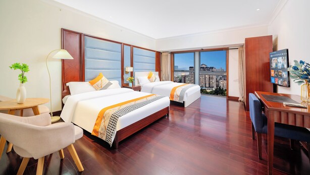 A hotel room with two beds, a desk, a chair, a lamp, and a view of the city. - Guangzhou Duoya Intl. Service Apartment (Guangzhou)