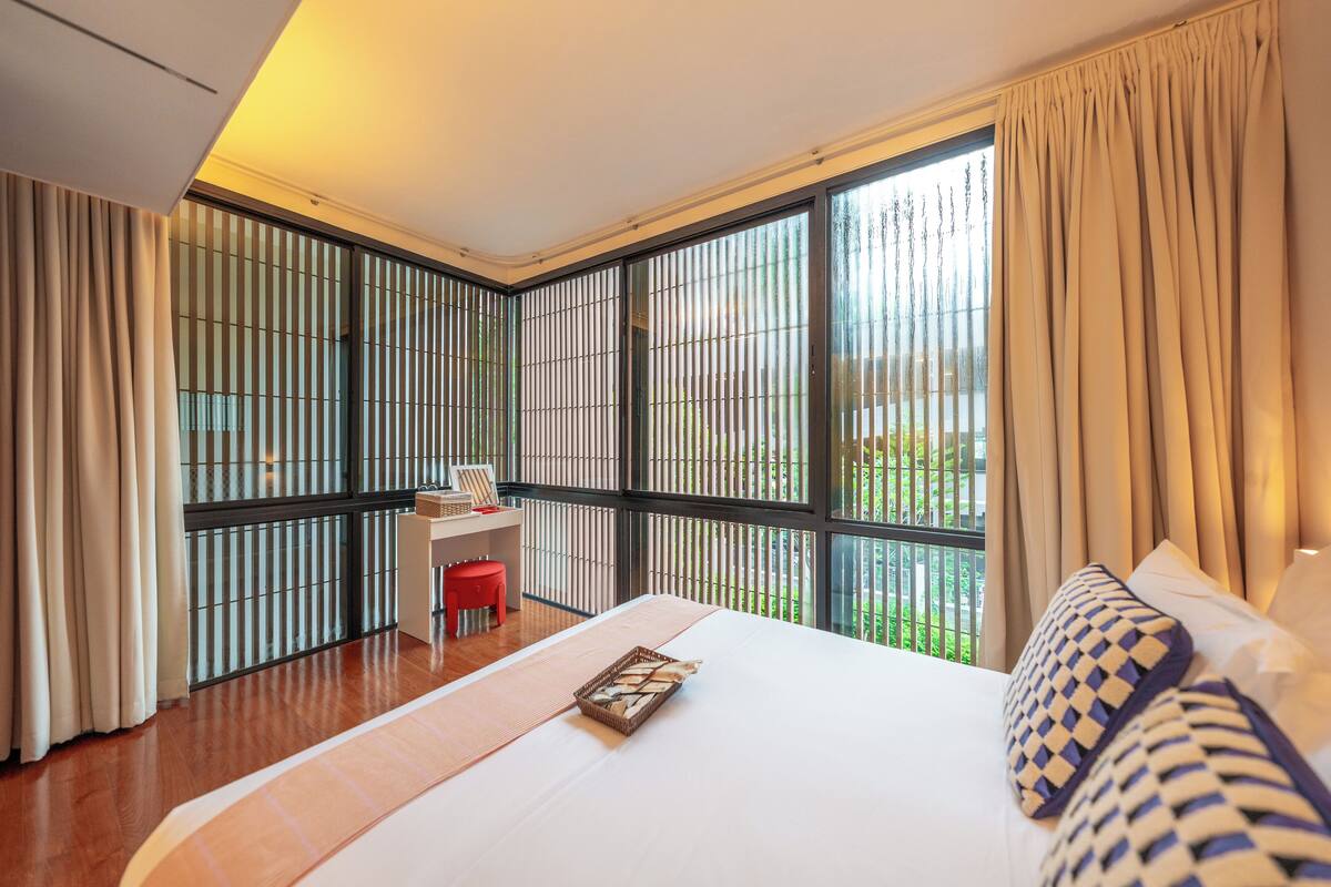 Une chambre d’hôtel avec un grand lit, un bureau avec une chaise et une vue dégagée grâce à de grandes fenêtres du sol au plafond.