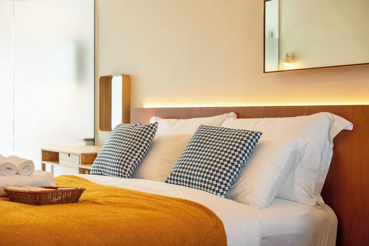 Une chambre d’hôtel avec un lit bien fait, une table de chevet et un grand miroir au mur.