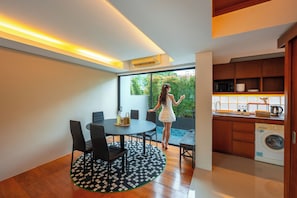 A modern kitchen with a built-in washer, a dining area with a round table and chairs, and a view of greenery through a large window. - Umi villa Pattaya  (Pattaya)