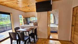 A cozy cabin with a wooden ceiling, a dining area with a table and chairs, a kitchen with a refrigerator and stove, and a bathroom with a bathtub. - Nature, confort and jacuzzi: New condo in Oxapampa - Villa Fortuna (Cantarizú)