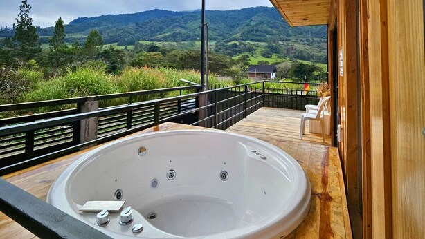 A wooden deck with a hot tub, overlooking a scenic landscape with hills and a cloudy sky. - Nature, confort and jacuzzi: New condo in Oxapampa - Villa Fortuna (Cantarizú)