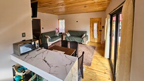 A cozy room with a wooden ceiling, two green sofas, a marble table, and a TV on a stand. - Nature, confort and jacuzzi: New condo in Oxapampa - Villa Fortuna (Cantarizú)