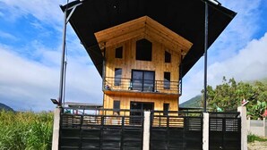 A wooden cabin with a balcony, surrounded by a metal fence and set against a mountainous backdrop. - Nature, confort and jacuzzi: New condo in Oxapampa - Villa Fortuna (Cantarizú)
