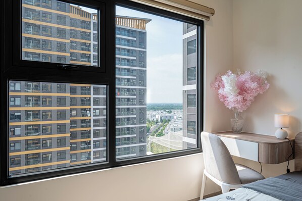 A hotel room with a large window, a desk with a chair, and a vase of flowers.