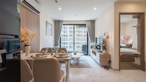A modern living room with a dining area, a TV, and a large window with curtains. - LA Nest - Vena Nest (Ho Chi Minh City)