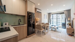 A modern kitchen with a built-in refrigerator, a dining area with a table and chairs, and a large window offering a city view. - LA Nest - Vena Nest (Ho Chi Minh City)