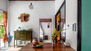 Una habitación con una mesa de madera, un frutero, un florero con flores, un armario verde y una lámpara colgante.