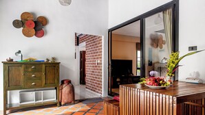 Una habitación con un armario de madera, suelo de baldosas, pared de ladrillo, puerta de vidrio corredera y una mesa con fruta.
