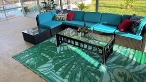 Un espace extérieur aménagé, abrité et doté d’un canapé d’angle, d’une table basse en verre et de plantes en pot.
