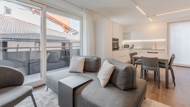 En moderne lejlighed med en grå sofa, et spisebord og et køkkenområde.