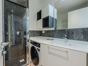 Un baño moderno con ducha envuelta en vidrio, lavadora integrada y tocador blanco con espejo.
