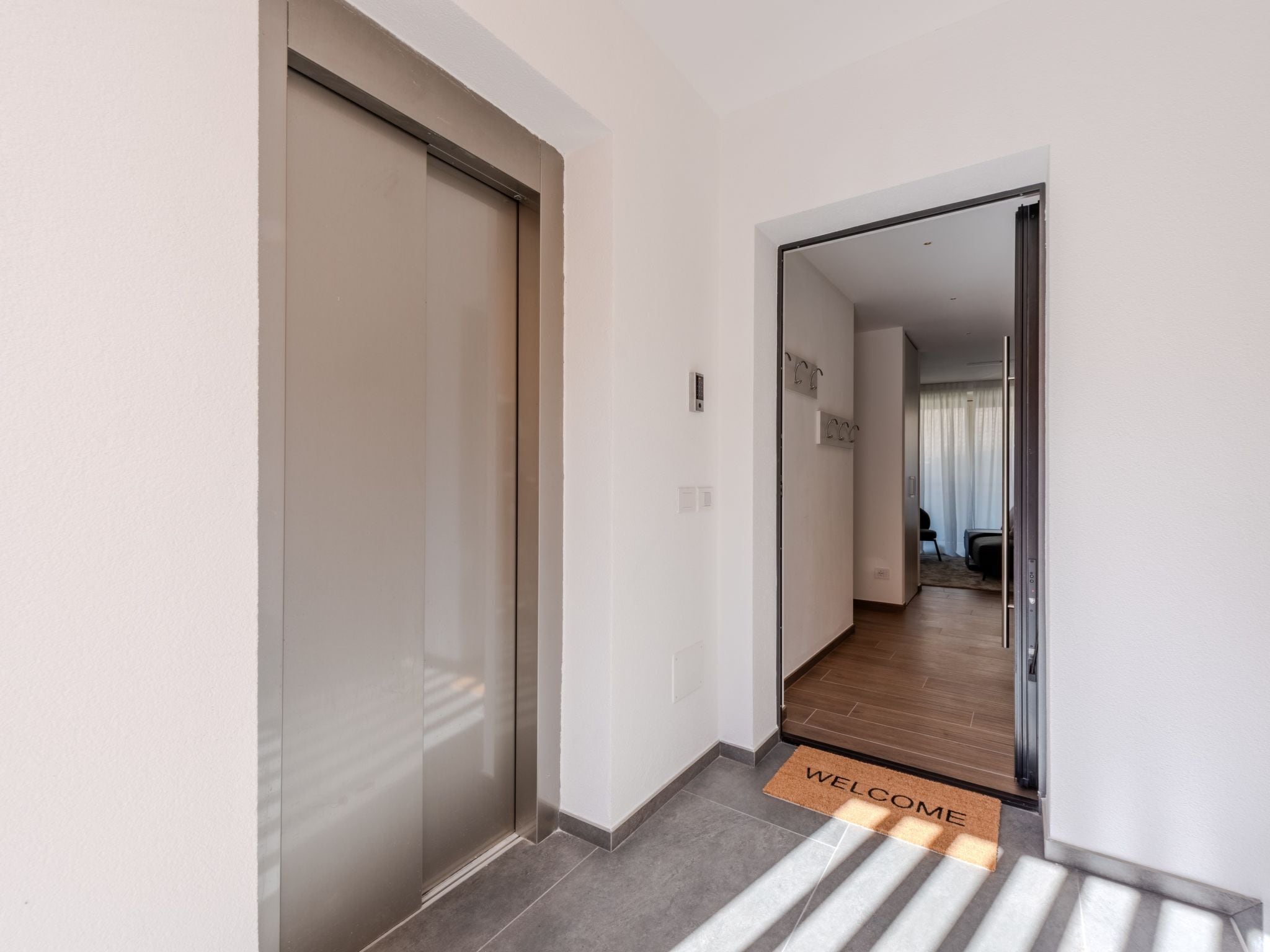Un pasillo moderno con una puerta corredera, un felpudo y vistas a una habitación con cama y cortinas.