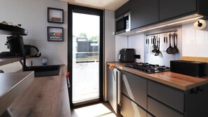 A modern kitchen with a wooden countertop, a stove, a microwave, and a sink. There are framed pictures on the wall and a window with a view of the outside. - Houseboat With Sauna and Fantastic View (Offingawier)
