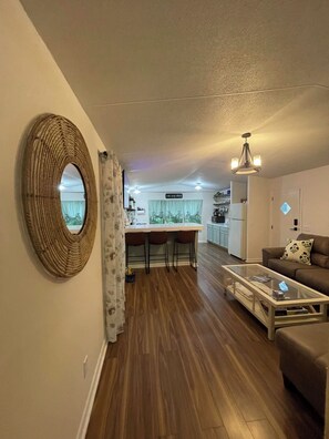 A modern living room with a glass coffee table, a brown sofa, and a dining area with a bar stool. - The Ouachita Nook-home near lake and crystal digging, in the heart of Mount Ida! (Mount Ida)