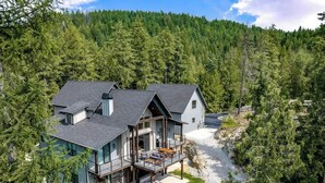 A modern two-story house with a large deck, surrounded by dense forest. - Extraordinary Idaho Club Retreat w/ Hot Tub (Sandpoint)