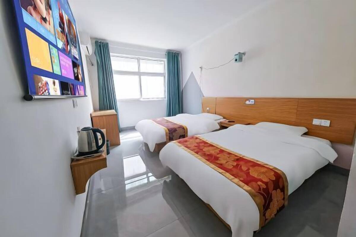 A hotel room with two beds, a coffee maker, a wall-mounted TV, and a window with curtains.