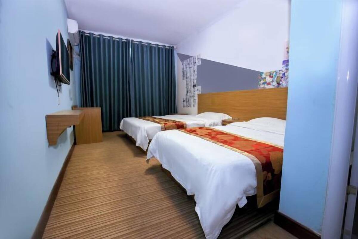 A hotel room with two beds, a desk, a TV, and a curtain.