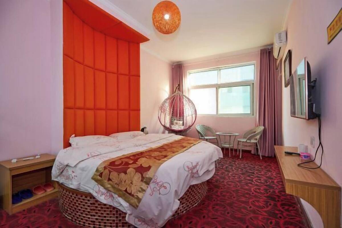 A hotel room with a bed, a hanging chair, a desk, and a window.