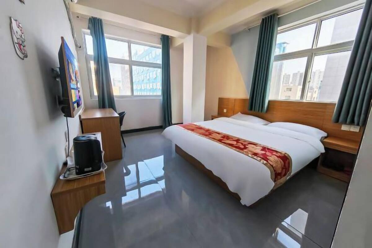 A hotel room with a large bed, a bedside table, a TV, and a window with curtains.