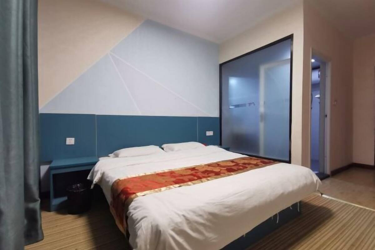 A hotel room with a bed, a nightstand, a wall-mounted TV, and a door leading to another room.