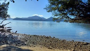 A pebbly beach with a calm lake, distant mountains, and trees framing the view.